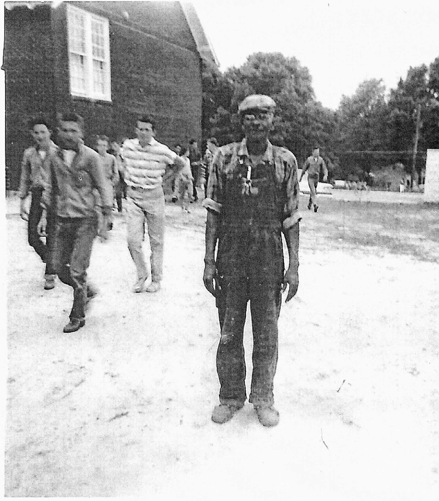 Otis Phillips standing on the Lyons High School grounds, with students and a school building behind him.